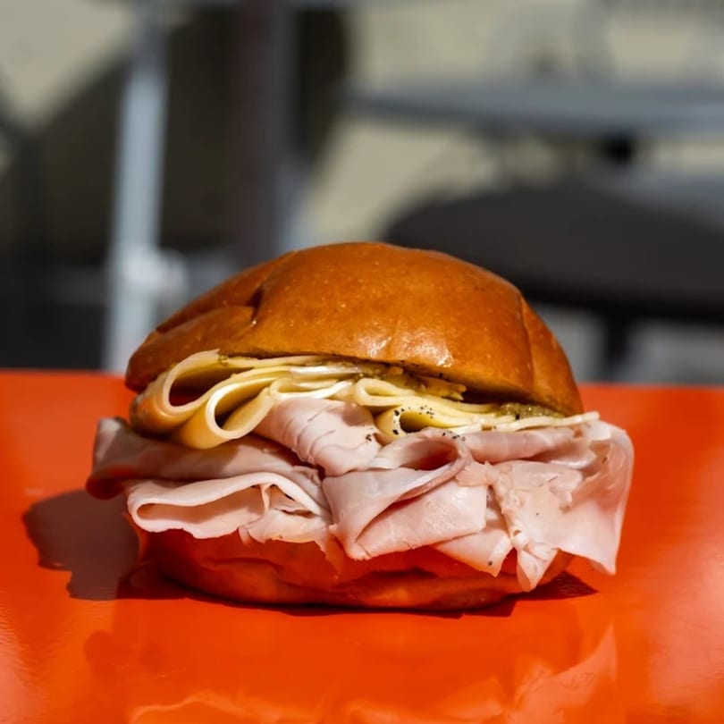 A deli sandwich with thinly sliced meat and cheese on a bun, on a bright orange surface.