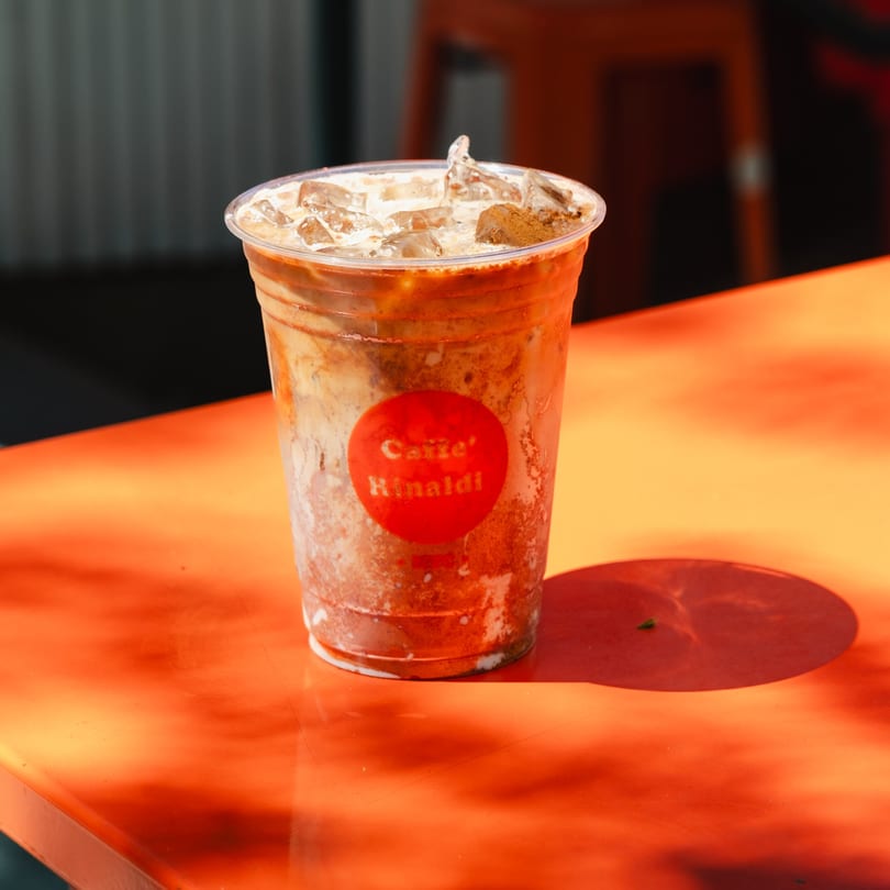 Iced coffee with a red Caffe' Rinaldi logo on a bright orange table.