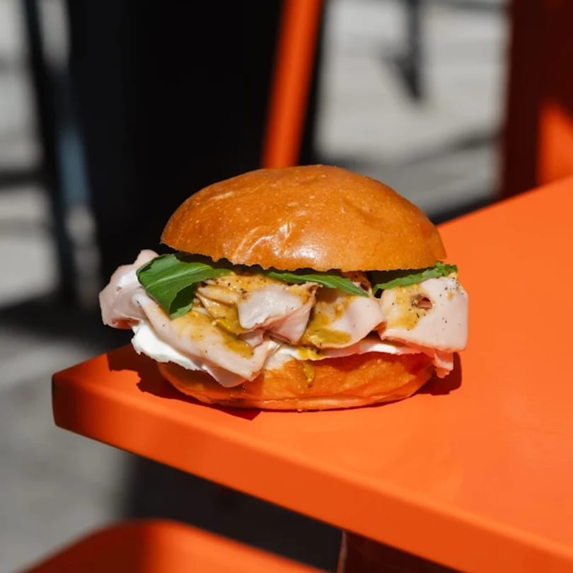 A turkey and arugula sandwich with mustard and cream cheese on a brioche bun.